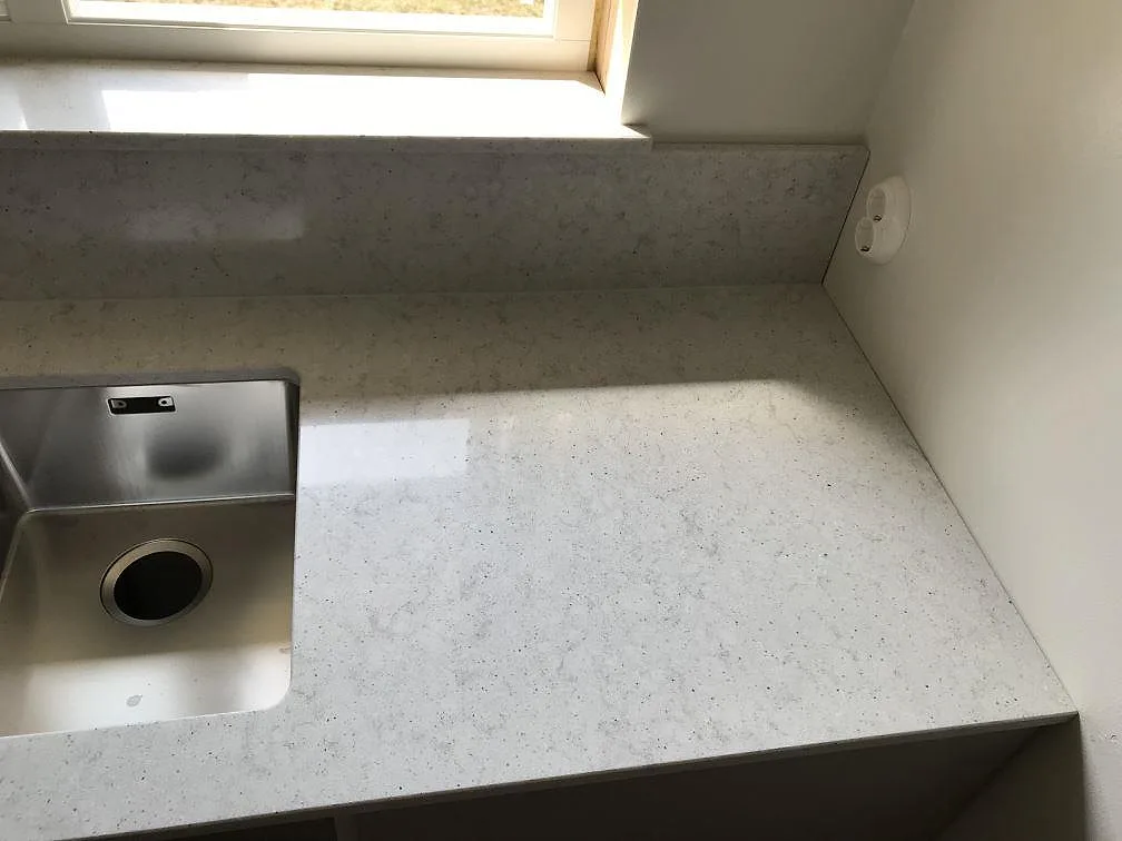 Köksbänkskiva i ljus Quarella Bianco Savoia komposit med underlimmad rostfri diskho och stenklädd fönsterbänk i Beddingestrand.