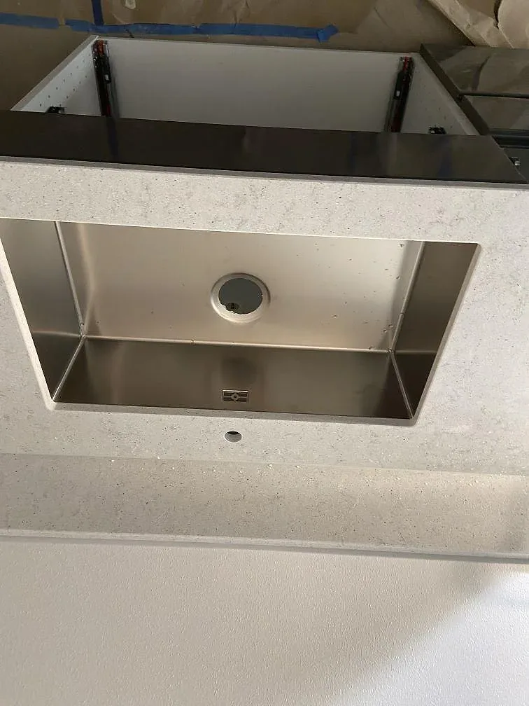 Underlimmad rostfri diskho och blandarehål i en köksbänkskiva av vit Quarella Bianco Savoia kvartskomposit i Blekinge.