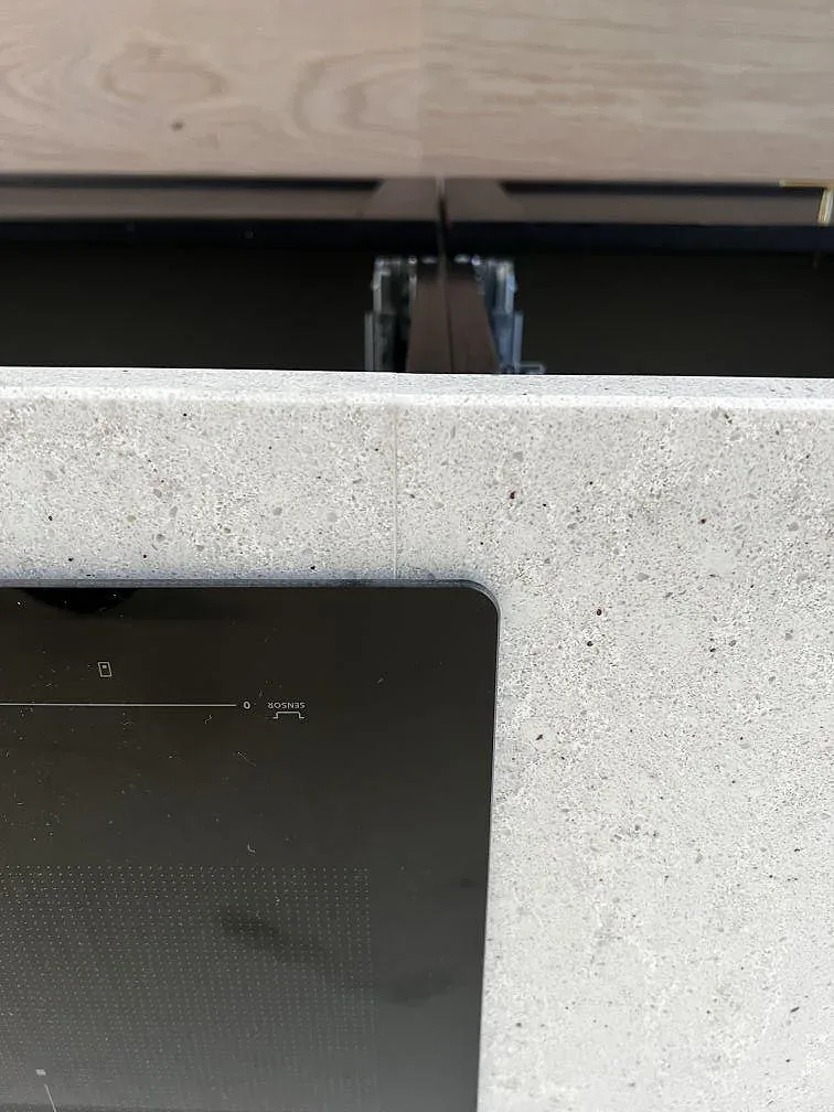 Detalj av infälld induktionshäll i polerad Quarella Bianco Savoia kvartskomposit i ett kök i Gantofta.
