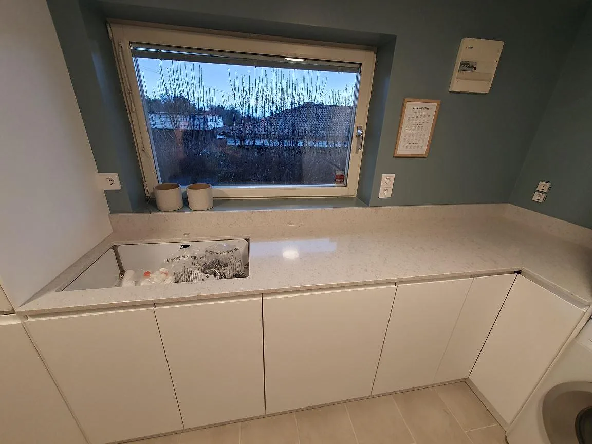 Polerad bänkskiva i ljus Quarella Bianco Savoia med fin, jämn ådring längs en fönstervägg i ett tvättrum i Hässelby.