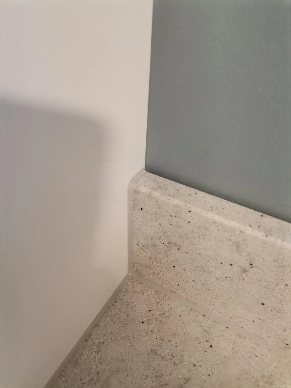 Detalj av den uppvikta stänkkanten i Quarella Bianco Savoia mot väggen i ett tvättrum i Hässelby.