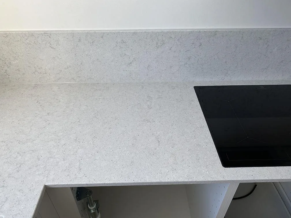 Köksbänkskiva i vit Quarella Bianco Savoia komposit med svart induktionshäll och fin diskret ådring i ett kök i Helsingborg.