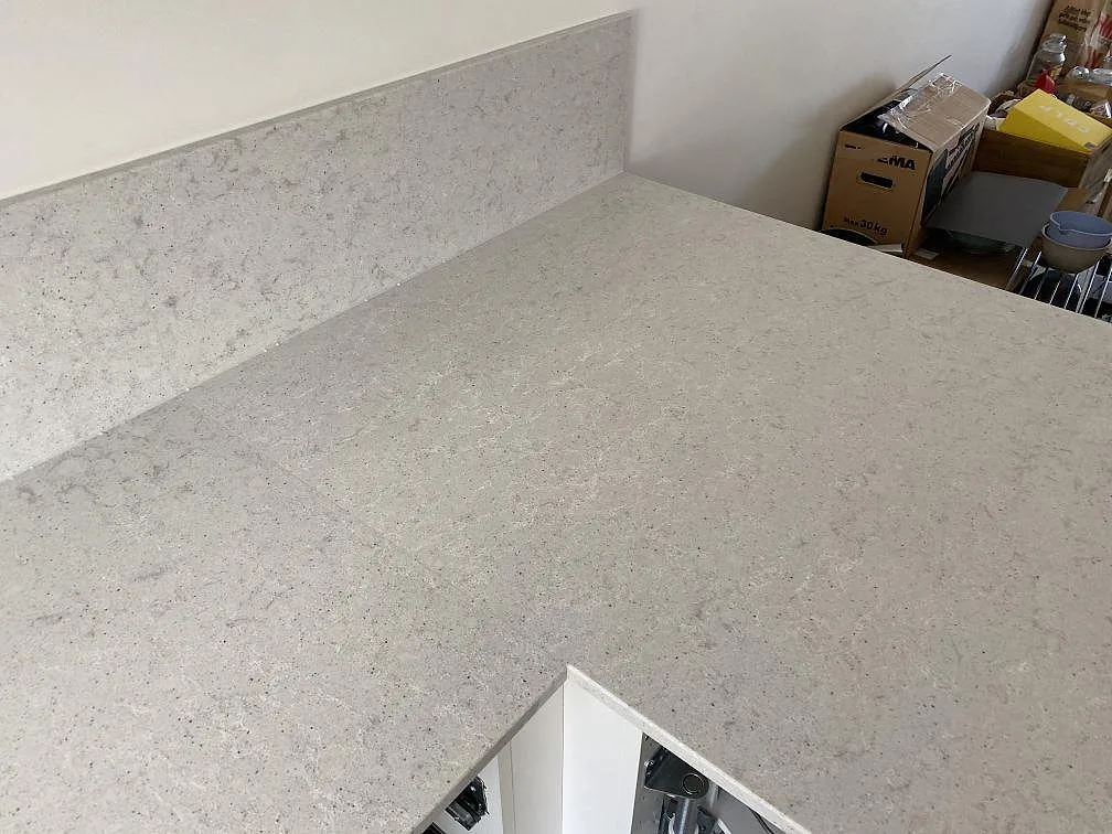 Hörnparti med uppvikt stänkkant i vit polerad Quarella Bianco Savoia komposit i ett kök i Helsingborg.