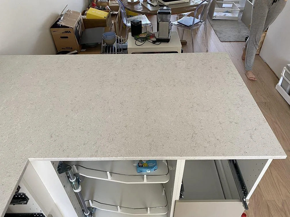 Rakt köksparti i vit Quarella Bianco Savoia komposit, polerad bänkskiva, fotograferat under montering i Helsingborg.