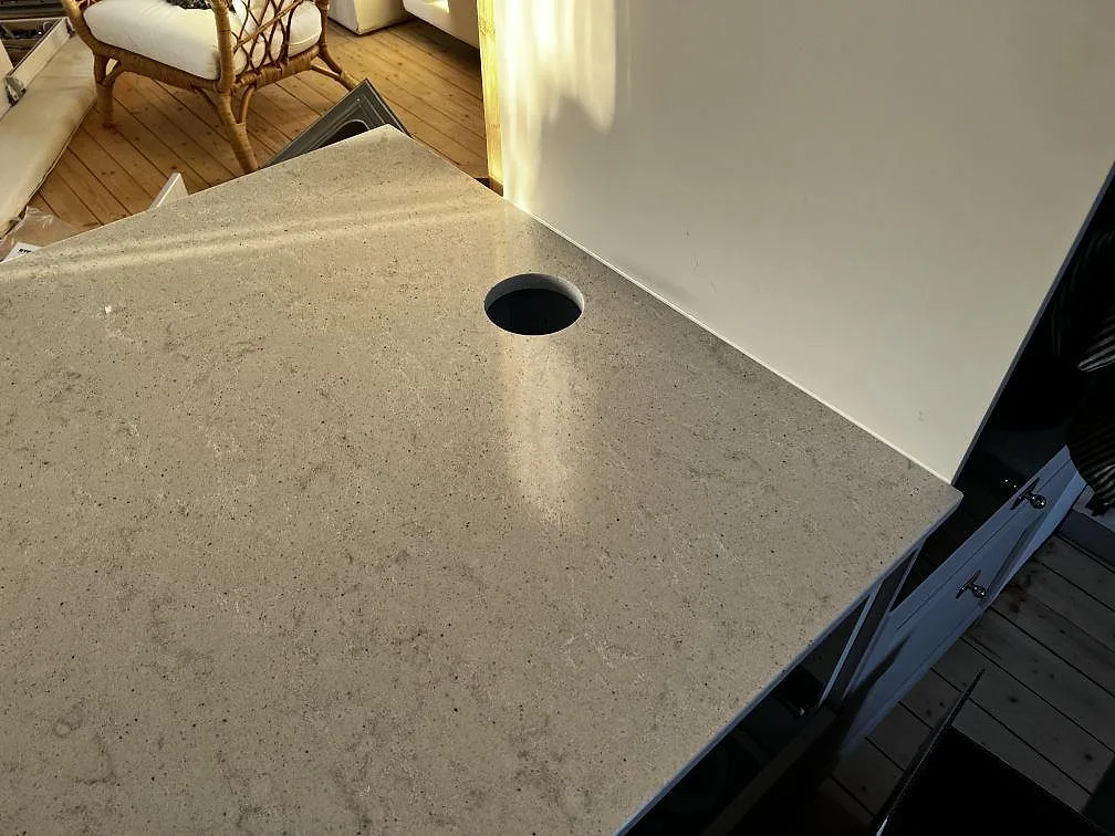 Detalj av polerad Quarella Bianco Savoia köksbänkskiva med kabelhål vid kökshalvö i Lomma.