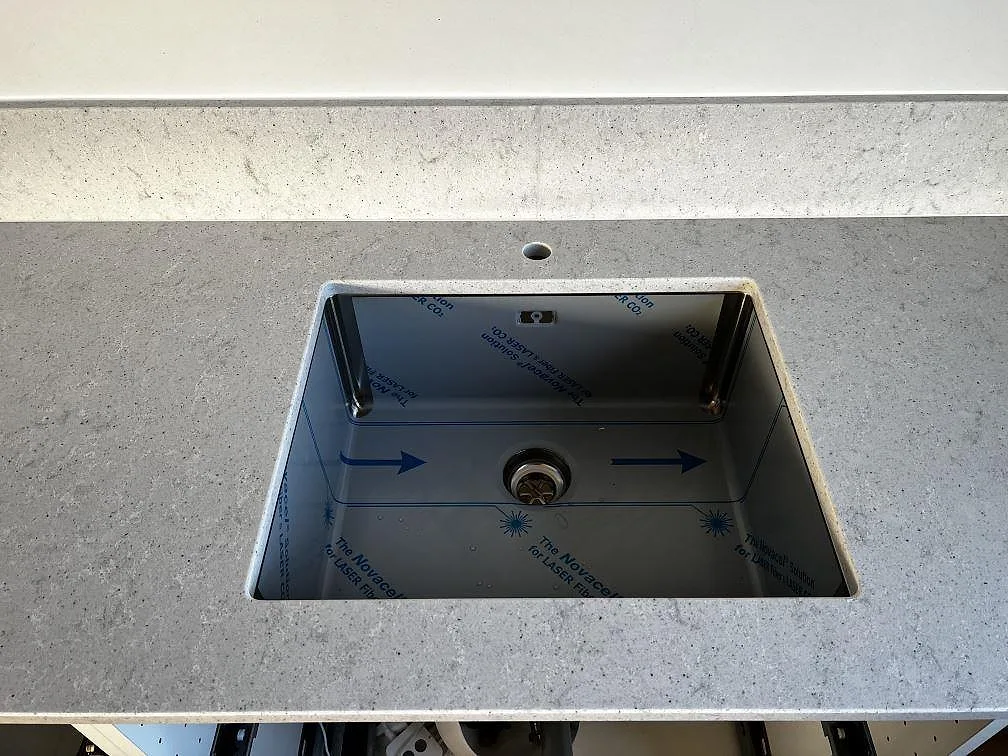 Närbild på underlimmad rostfri diskho i polerad Quarella Bianco Savoia bänkskiva med stänkkant i Lomma.