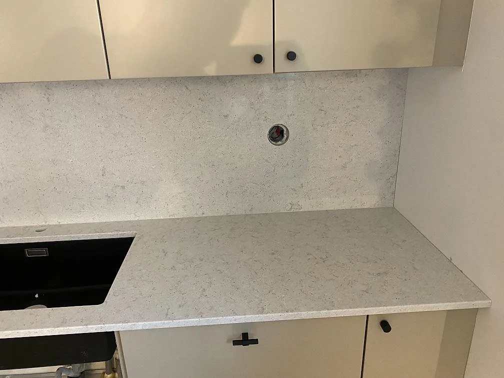 Polerad köksbänkskiva i Quarella Bianco Savoia med svart underlimmad kompositdiskho och uppdragen stänkvägg i samma sten i ett kök i Malmö.