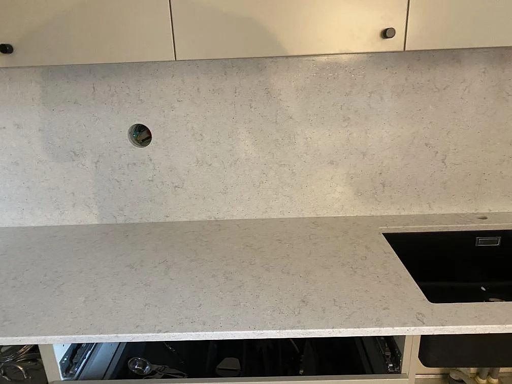 Köksbänkskiva i Quarella Bianco Savoia, ljus polerad komposit, med underlimmad diskho och heltäckande stänkskydd i ett kök i Malmö.