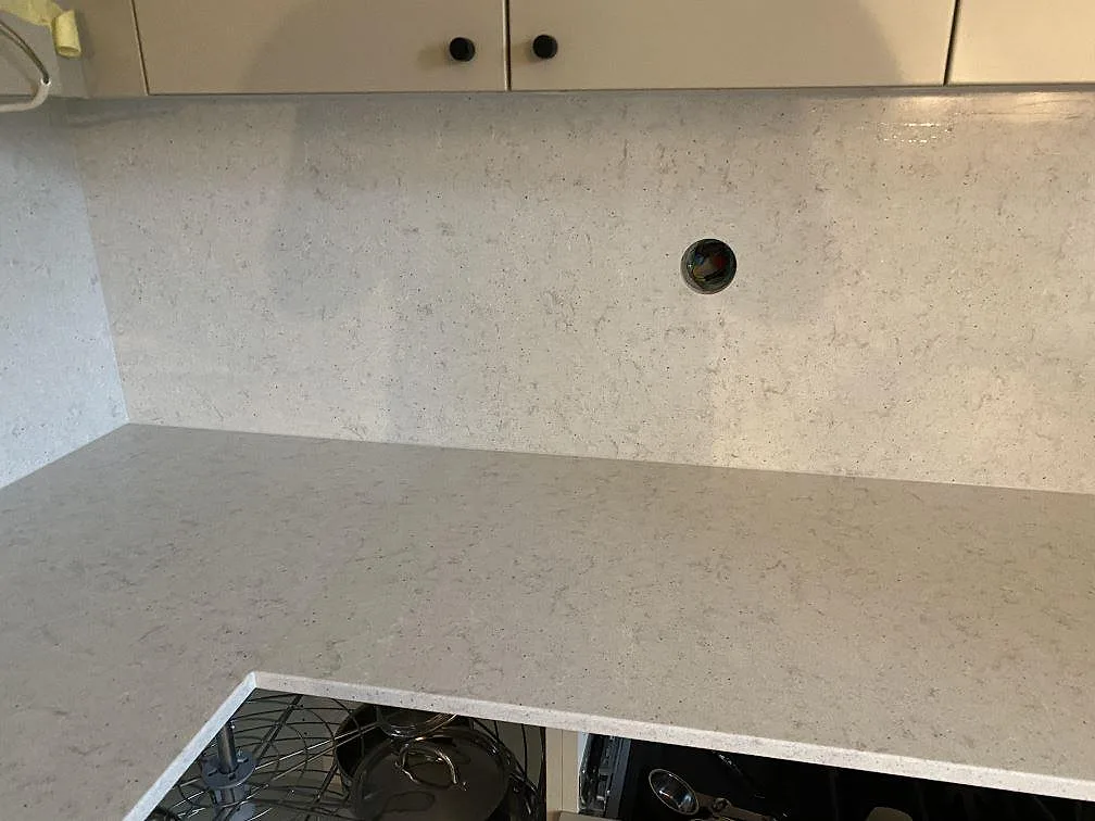 Köksbänkskiva i Quarella Bianco Savoia, ljus komposit med diskret grå ådring, med öppet underskåp under montering i ett kök i Malmö.