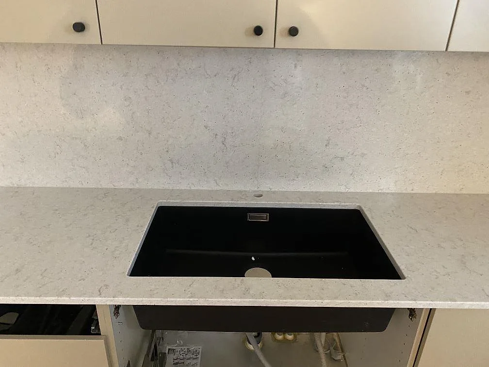 Närbild på den svarta underlimmade kompositdiskhon i Quarella Bianco Savoia köksbänkskiva, polerad ljus komposit med fin grå ådring, i Malmö.