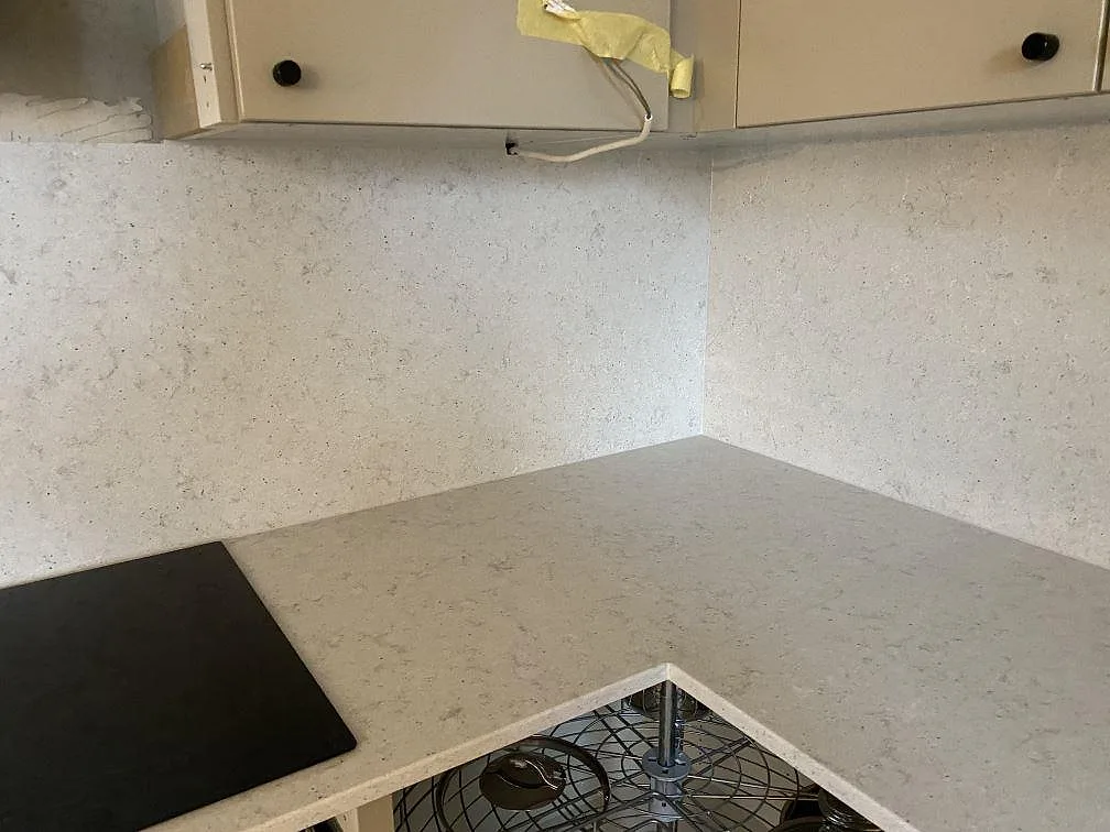 Hörnparti av L-formad köksbänkskiva i Quarella Bianco Savoia komposit med svart häll och heltäckande stänkvägg i ett kök i Malmö.