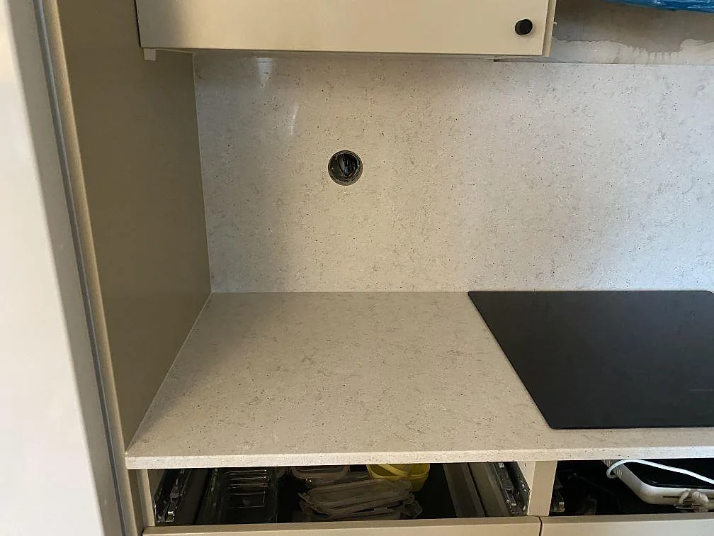 Köksbänkskiva i ljus Quarella Bianco Savoia komposit med svart induktionshäll och uppdragen stänkvägg i ett kök under montering i Malmö.