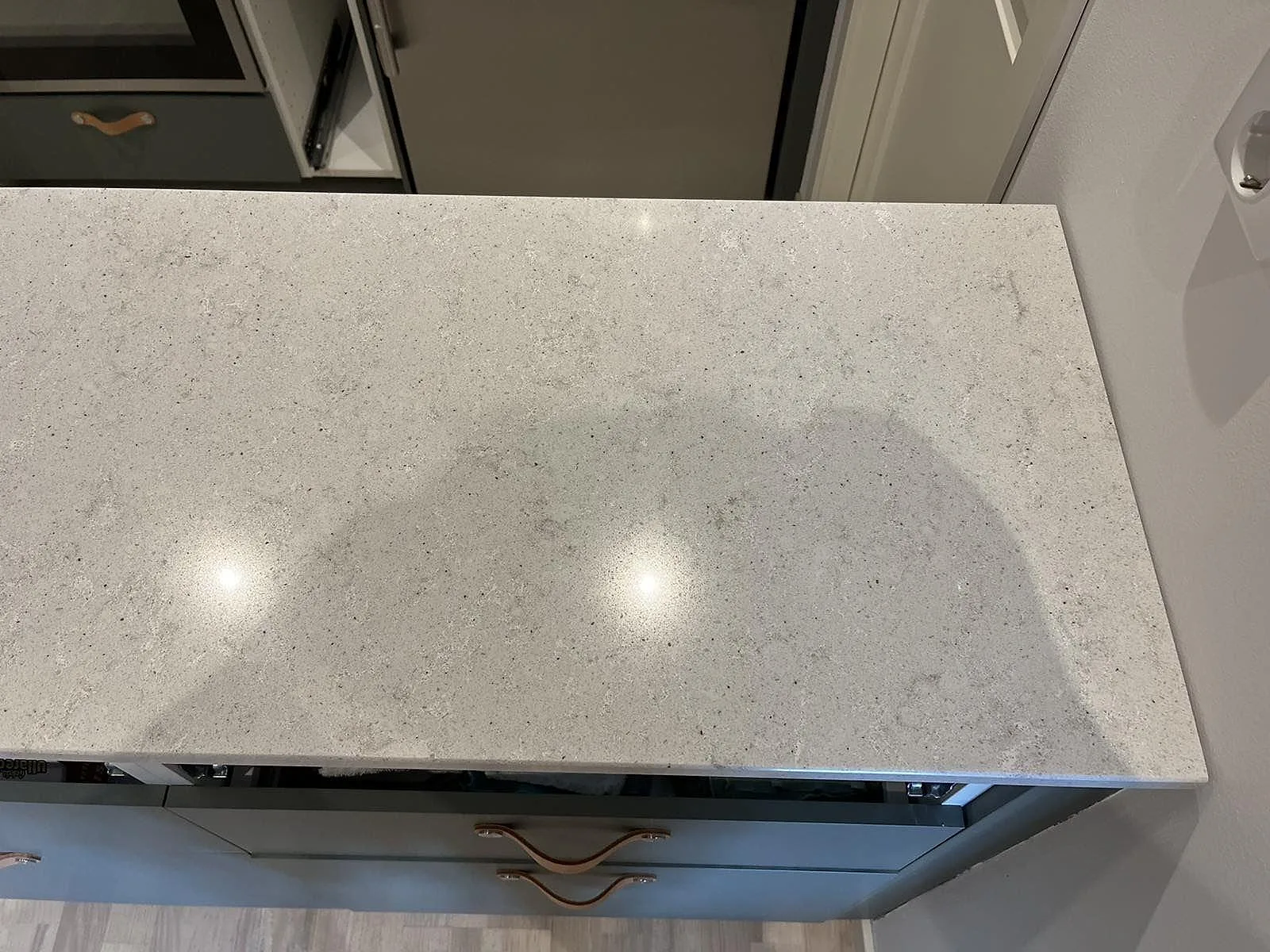 Polerad köksbänkskiva i ljus Quarella Bianco Savoia komposit ovanifrån, med spräcklig struktur, över gröna köksskåp i Malmö.
