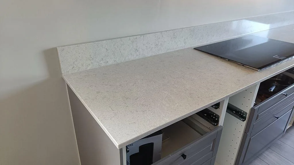 Vinklad vy av köksbänkskiva i ljus Quarella Bianco Savoia med fin spräcklig yta och uppvikt stänkkant i Nättraby.