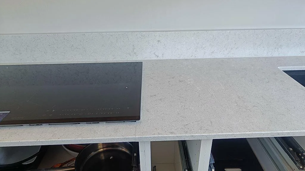 Närbild på infälld induktionshäll i polerad Quarella Bianco Savoia köksbänkskiva i Nättraby.