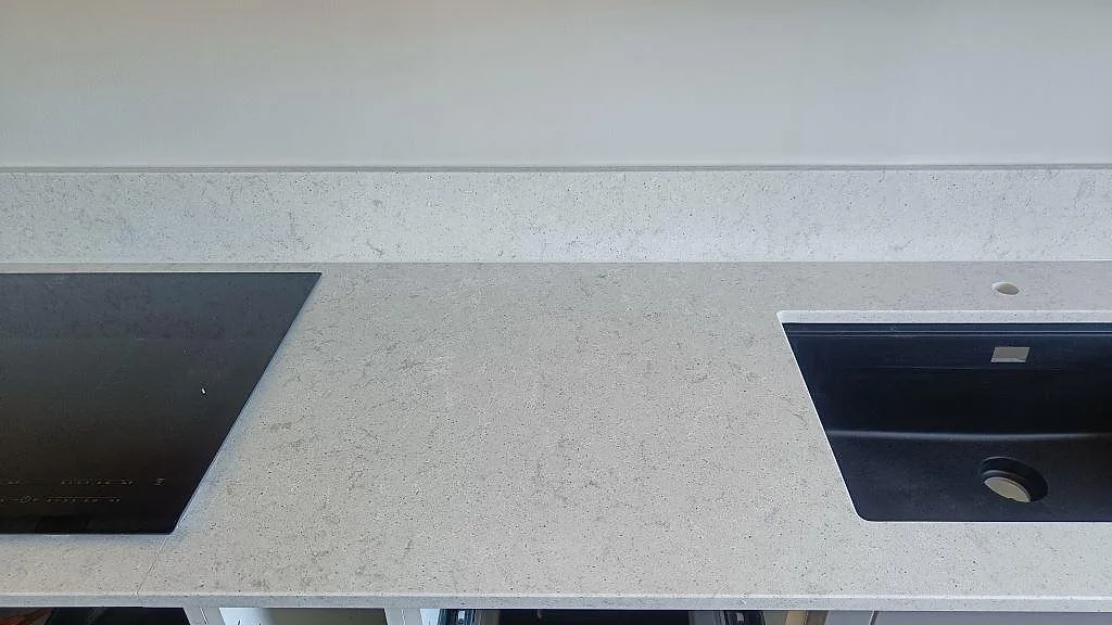 Polerad bänkskiva i Quarella Bianco Savoia med induktionshäll till vänster och underlimmad svart kompositdiskho till höger i ett kök i Nättraby.