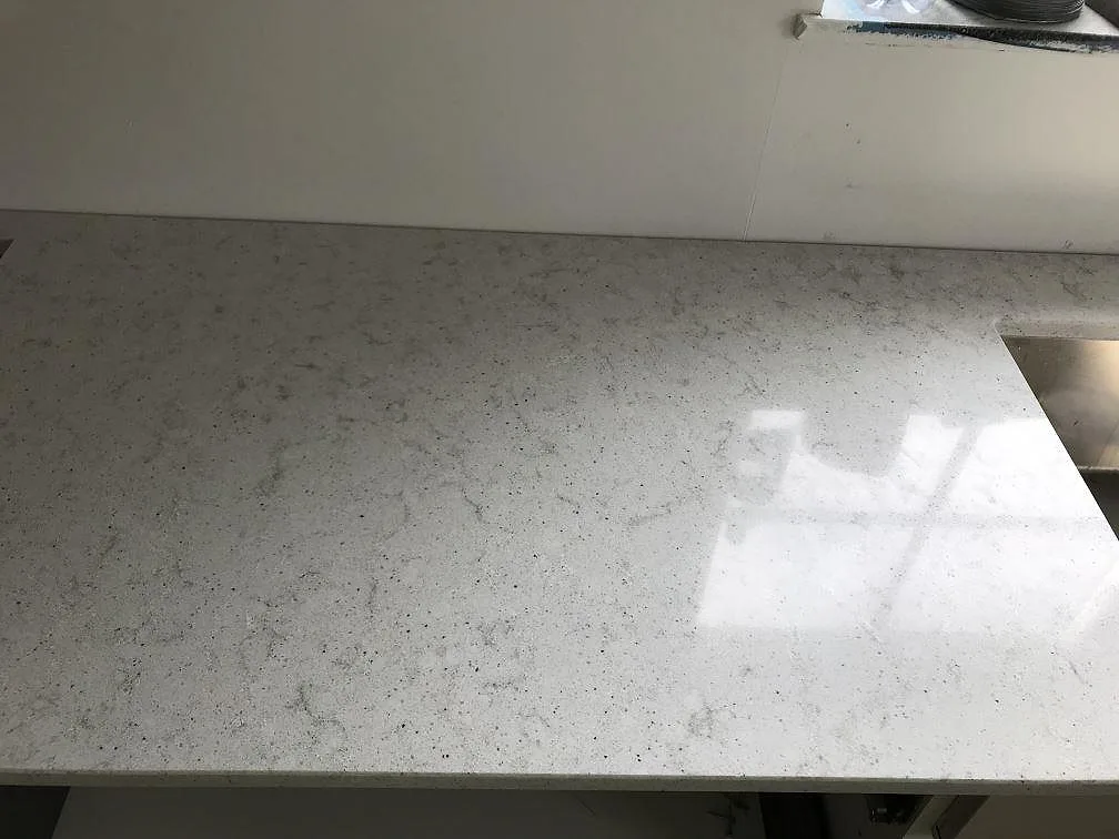 Polerad köksbänkskiva i Quarella Bianco Savoia med ljust melerad yta och solreflektion längs kanten i ett kök i Östra Grevie.
