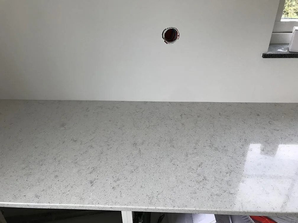 Köksbänkskiva i Quarella Bianco Savoia under fönstret, ljus kvartskomposit med polerad yta i ett kök i Östra Grevie.