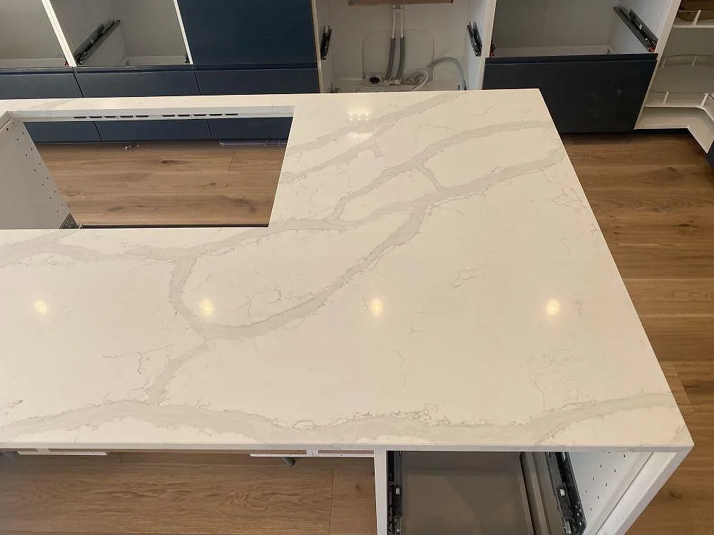 Köksö i polerad Quarella Bianco Venere komposit med tydlig grå ådring och underlimmad rostfri diskho i ett kök i Påarp.