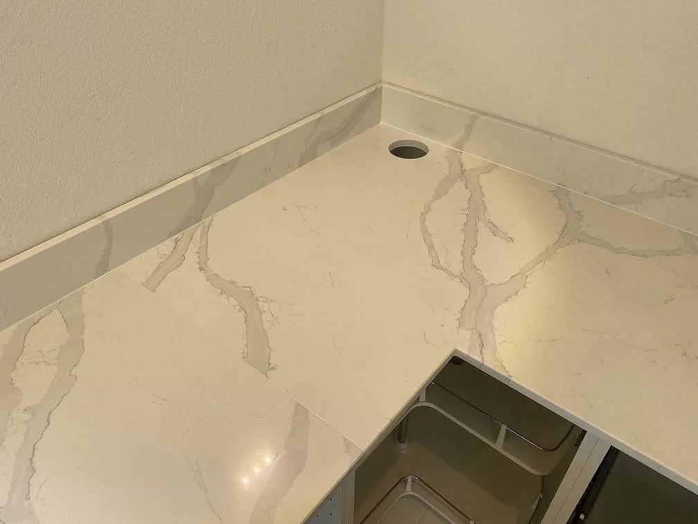 Hörnparti av köksbänkskiva i Quarella Bianco Venere komposit med uppvikt kant och blandarhål i ett kök i Påarp.