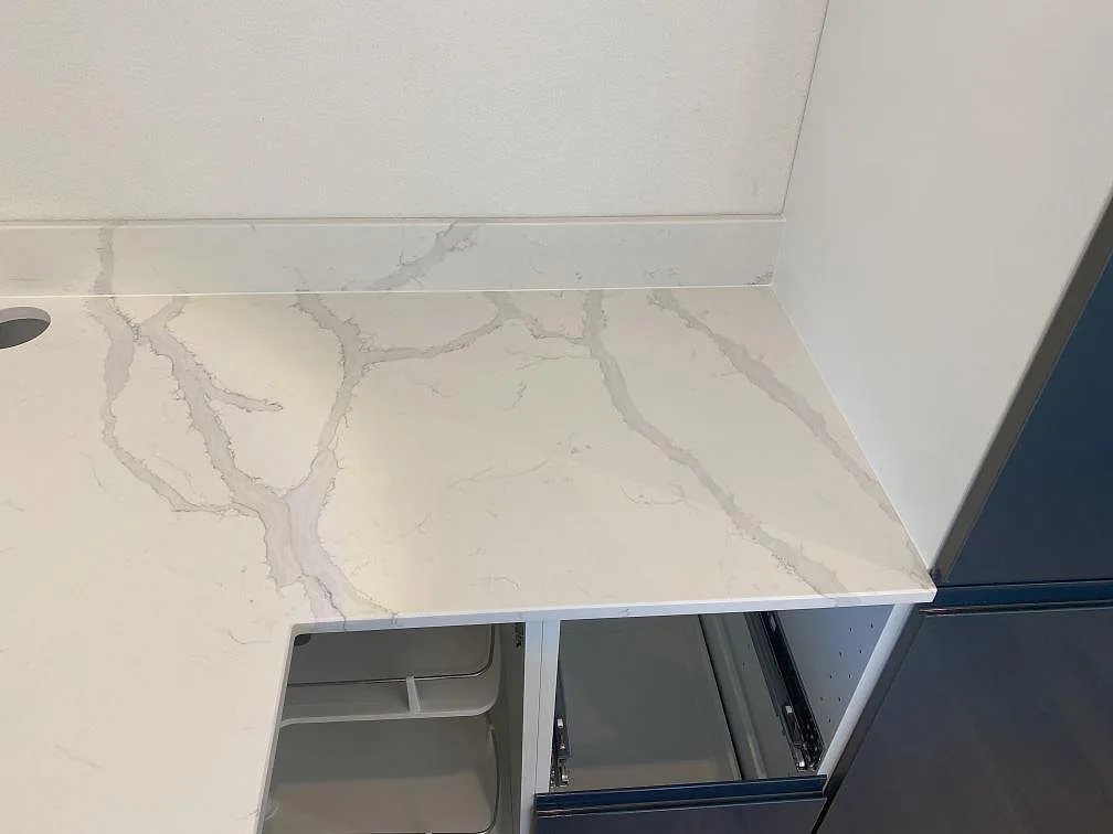 Bänkskiva i vit Quarella Bianco Venere med grå ådring och hål för blandare i ett kök i Påarp.