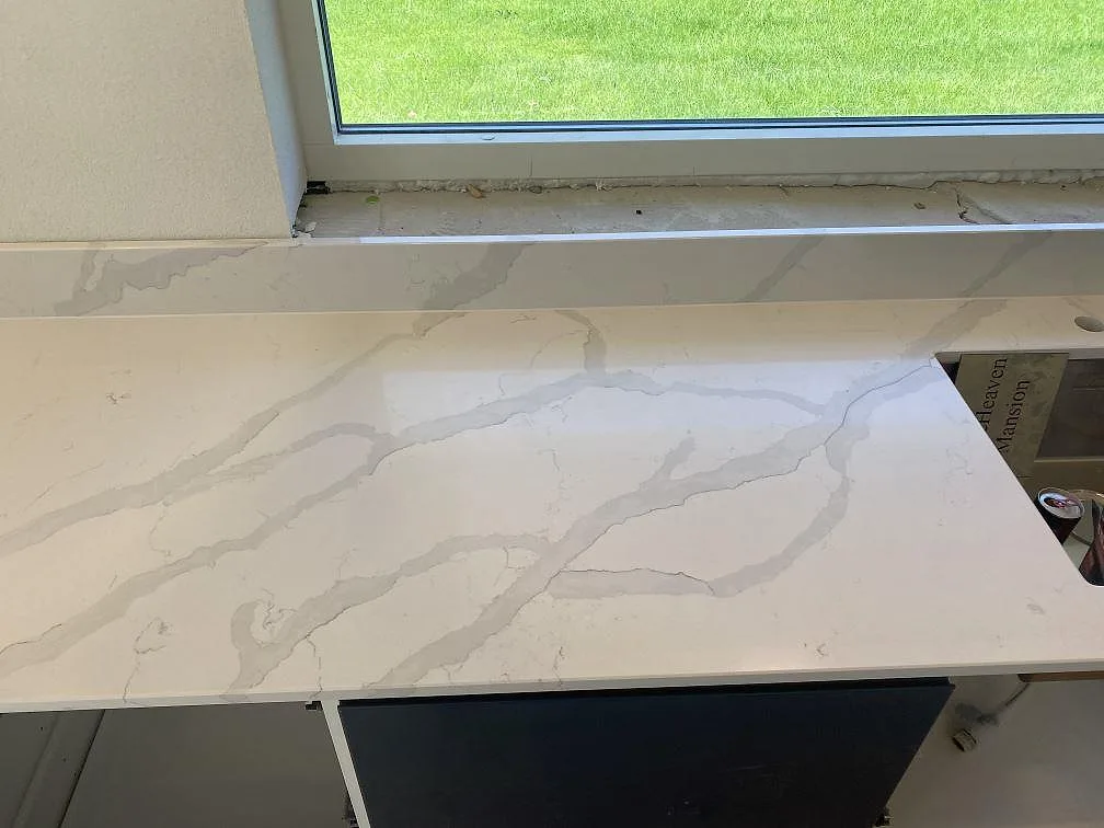Polerad köksbänkskiva i Quarella Bianco Venere med grå calacatta-ådring längs fönstervägg i ett kök i Påarp.