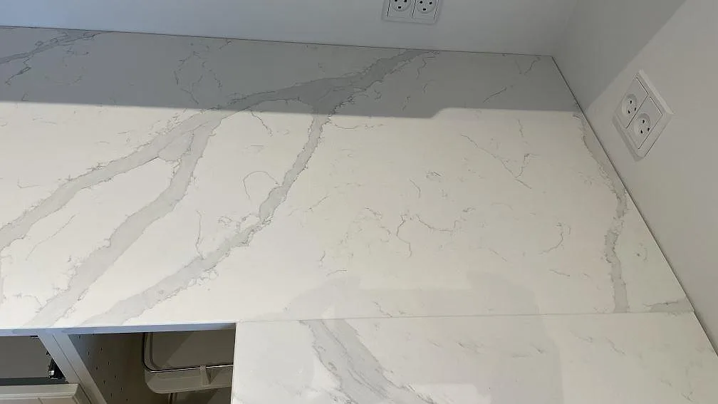 Köksbänkskiva i vit Quarella Bianco Venere, polerad agglomererad kvarts/marmorkomposit med grå ådring, i ett L-format kök i Rødovre.