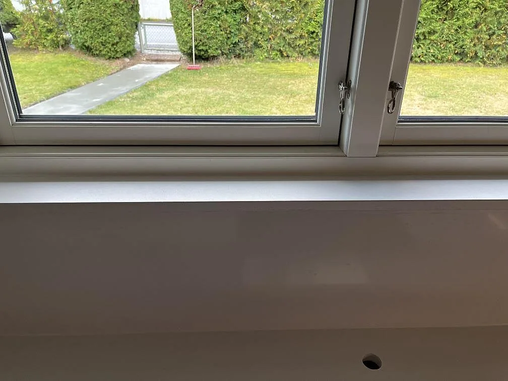 Polerad vit fönsterbänk i Quarella Blanco Sal under ett köksfönster med utsikt mot trädgården i Tjörnarp.