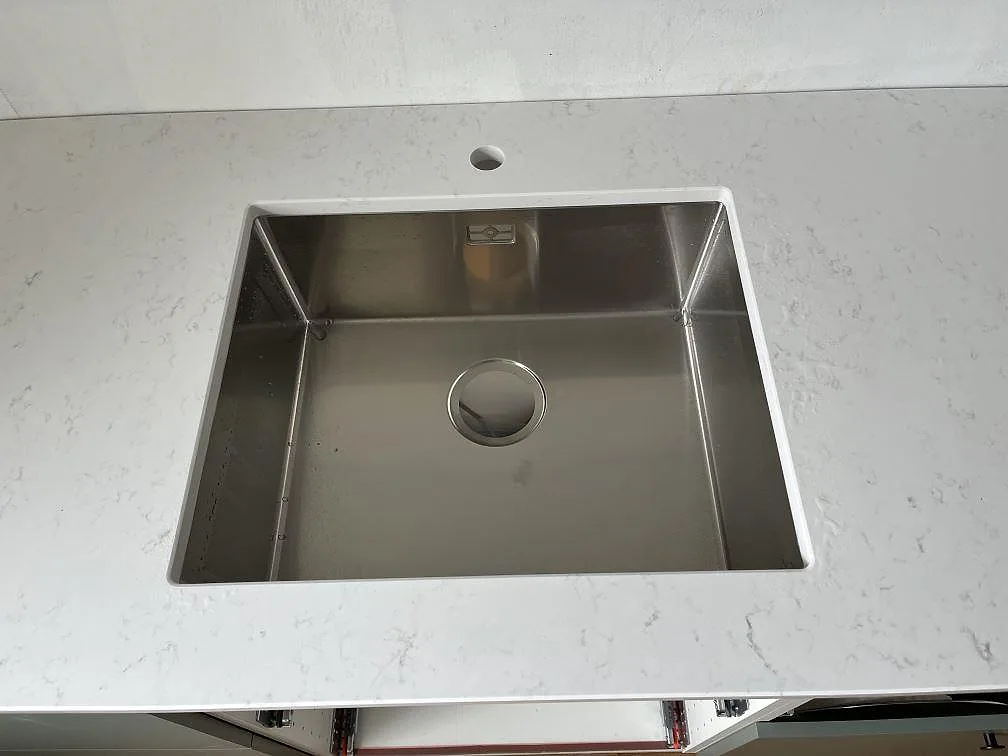 Underlimmad rostfri enkelho i köksbänkskiva av polerad Quarella Navona med separat blandarhål i ett kök i Klagshamn.