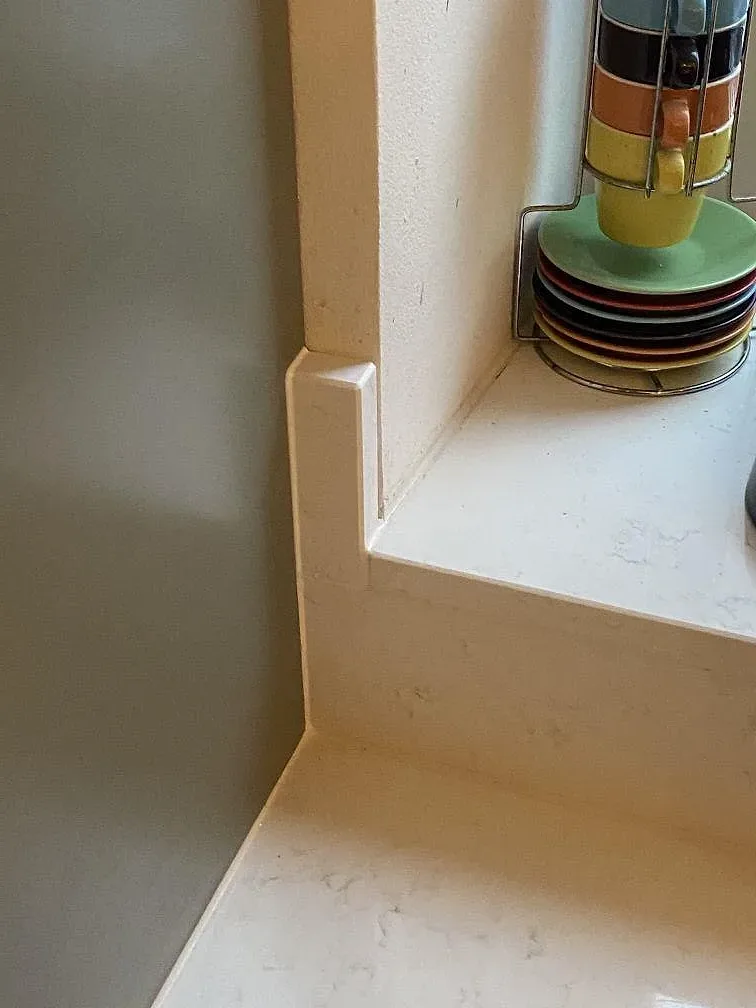 Detalj av polerad Quarella Navona köksbänkskiva med uppvikt kant och fönsternisch i ett kök i Limhamn.