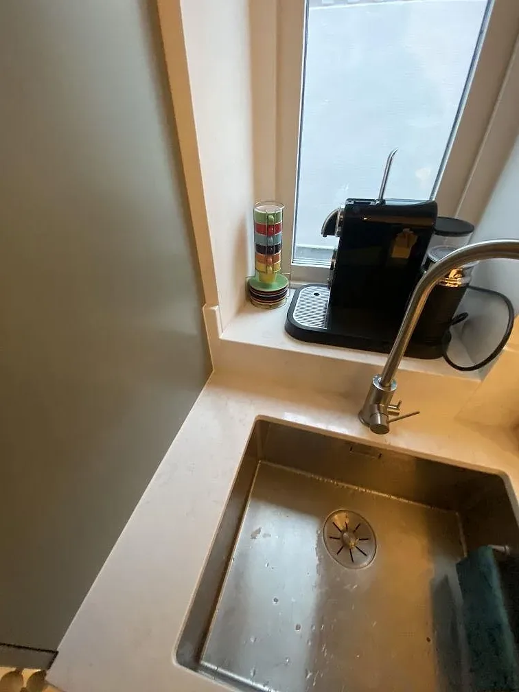 Köksbänkskiva i ljus Quarella Navona, polerad kvartskomposit, med rostfri diskho, blandare och fönsternisch i Limhamn.