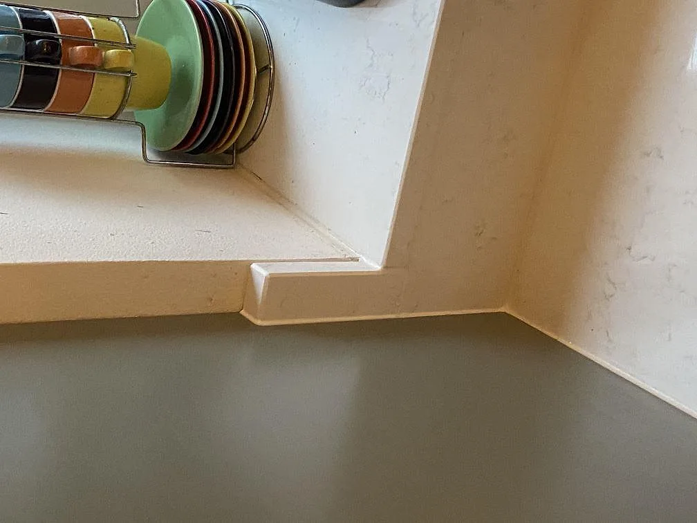 Fönsterbänk och stänkskydd i ljus Quarella Navona kvartskomposit, polerad, med profilerad kant och hörnvägg i ett kök i Limhamn.