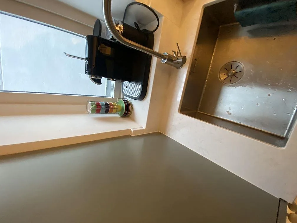 Köksvrå i Limhamn med ljus Quarella Navona som fönsterbänk och stänkskydd, polerad yta, intill diskho med köksblandare.