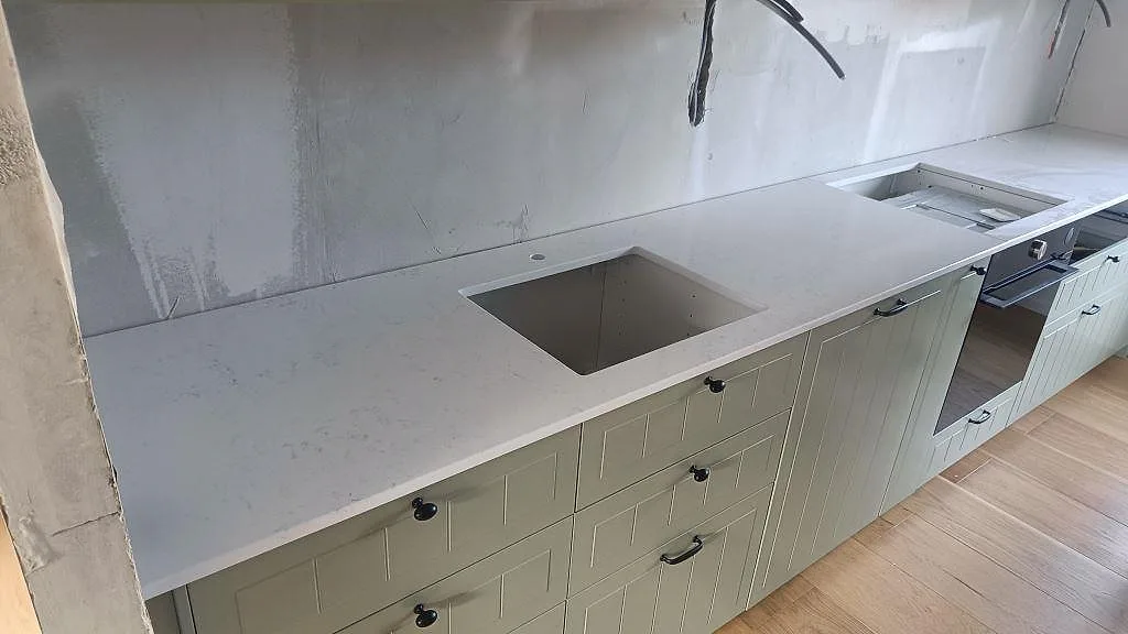 Köksbänkskiva i Quarella Navona, krämbeige komposit, polerad, med underlimmad diskho i ett kök under montering i Lund.