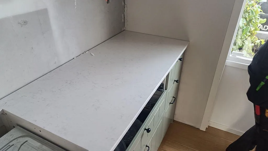 Krämbeige Quarella Navona bänkskiva i komposit längs en köksvägg vid fönster i Lund, polerad yta under montering.