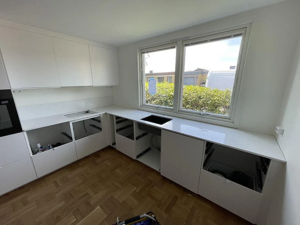 U-format kök i Malmö med polerad Quarella Navona, 20 mm komposit, monterad på vita stommar under stora fönster.