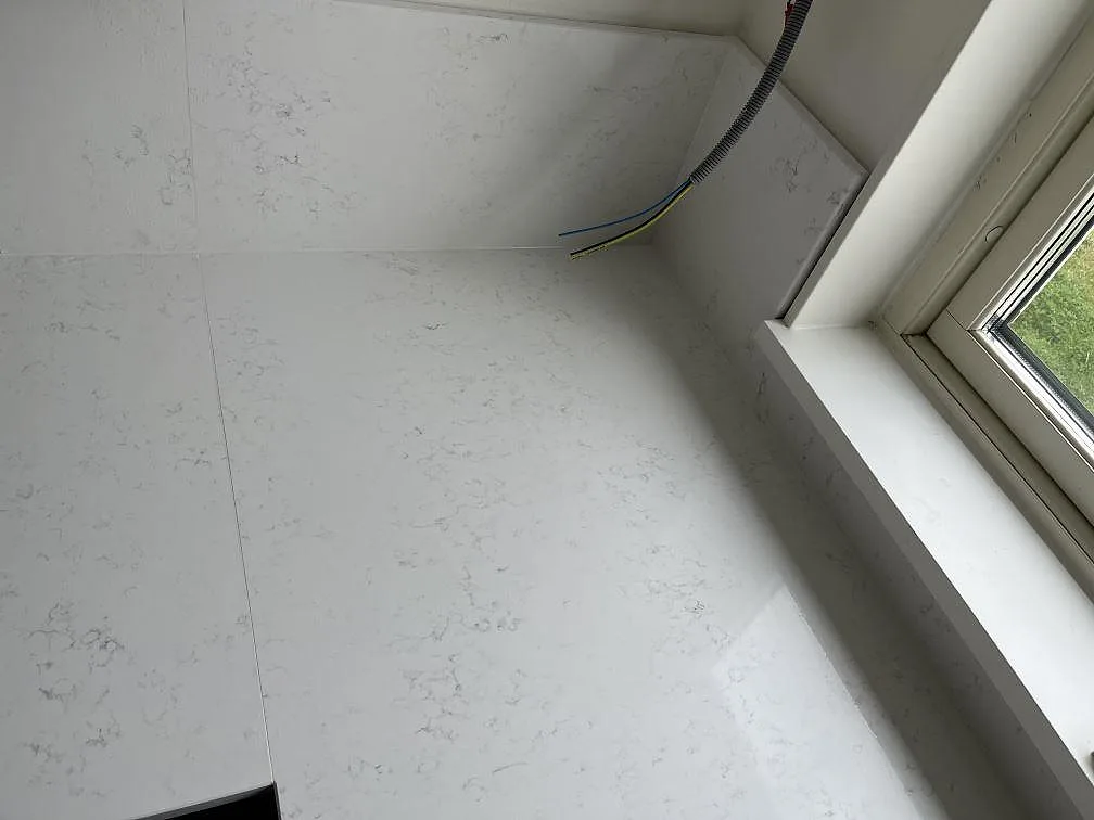 Vit Quarella Navona bänkskiva med stänkkant och mjuk grå ådring vid fönsterbänken i ett kök i Skurup.