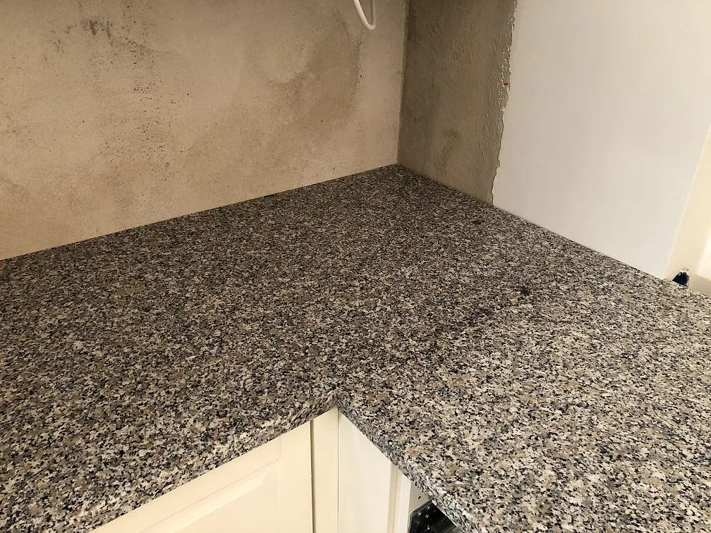 Köksbänkskiva i Rosa Beta granit mot en putsad vägg, med synlig kornig stenstruktur och rundad kant, i ett kök i Ängelholm.