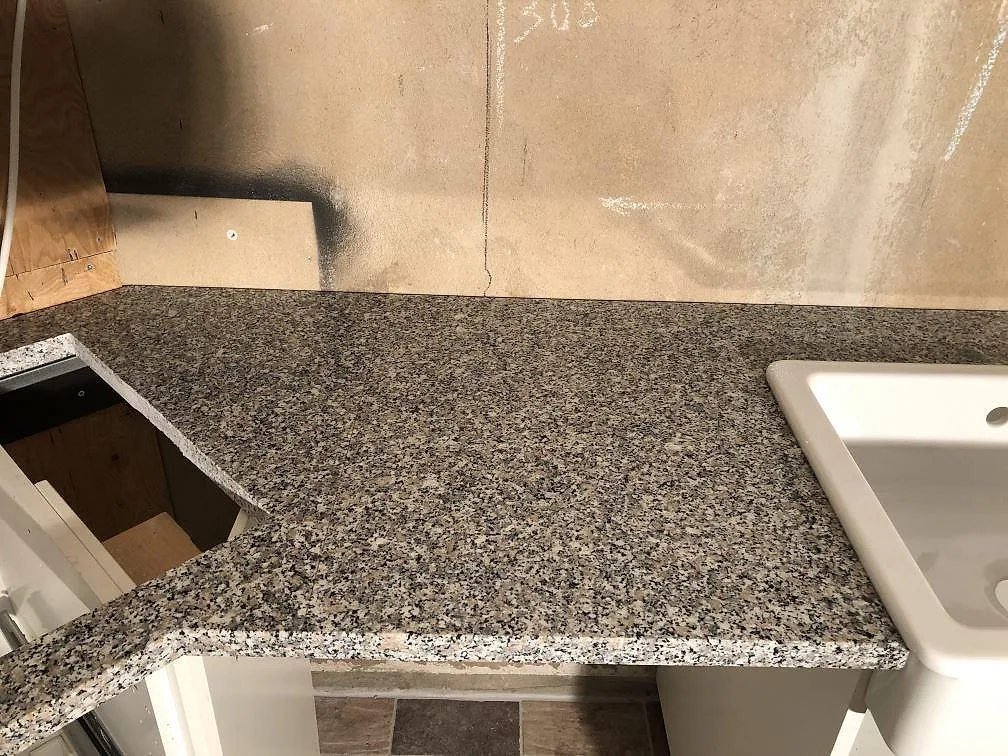Vit diskho av keramik placerad på en köksbänkskiva i Rosa Beta granit under installation i ett kök i Ängelholm.