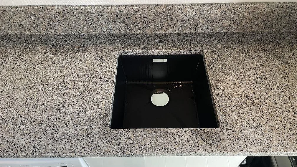 Närbild på svart drop-in-diskho monterad ovanpå en polerad Rosa Beta granitskiva i Hyllinge.