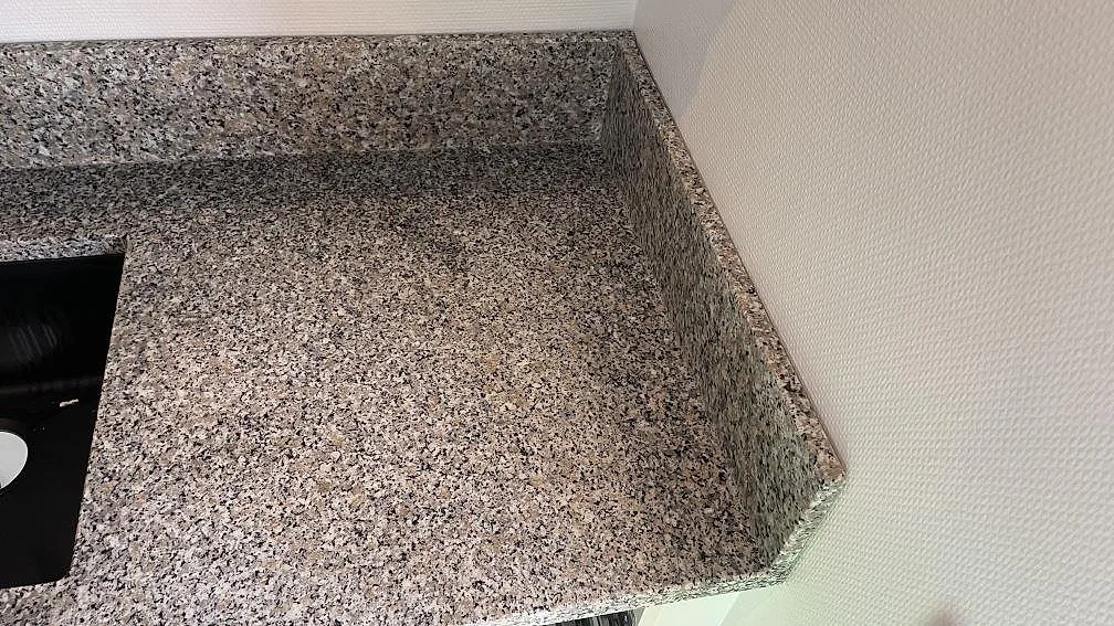 Sidodetalj av polerad Rosa Beta granit med uppvikt stänkkant och avslut mot vägg i Hyllinge.