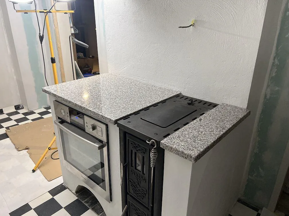 Polerad granitskiva i Rosa Beta runt spisdel och ugn i ett kök under montering i Nyköping.