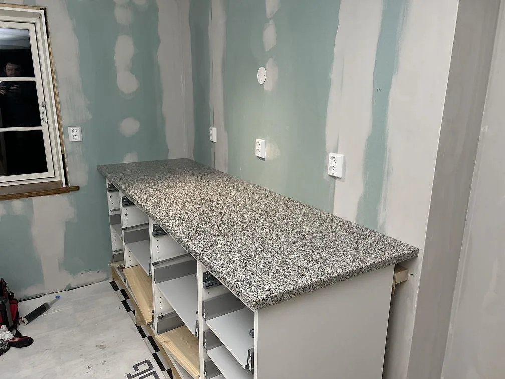 Lång polerad köksbänkskiva i granit Rosa Beta på öppna köksstommar i ett kök under montering i Nyköping.