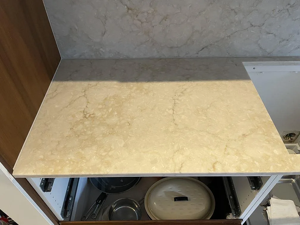 Närbild på den polerade Royal Beige-bänkskivan i beige kvartskomposit med mjuk ådring, mot en grå stenstänkvägg i ett kök under montering i Uppsala.