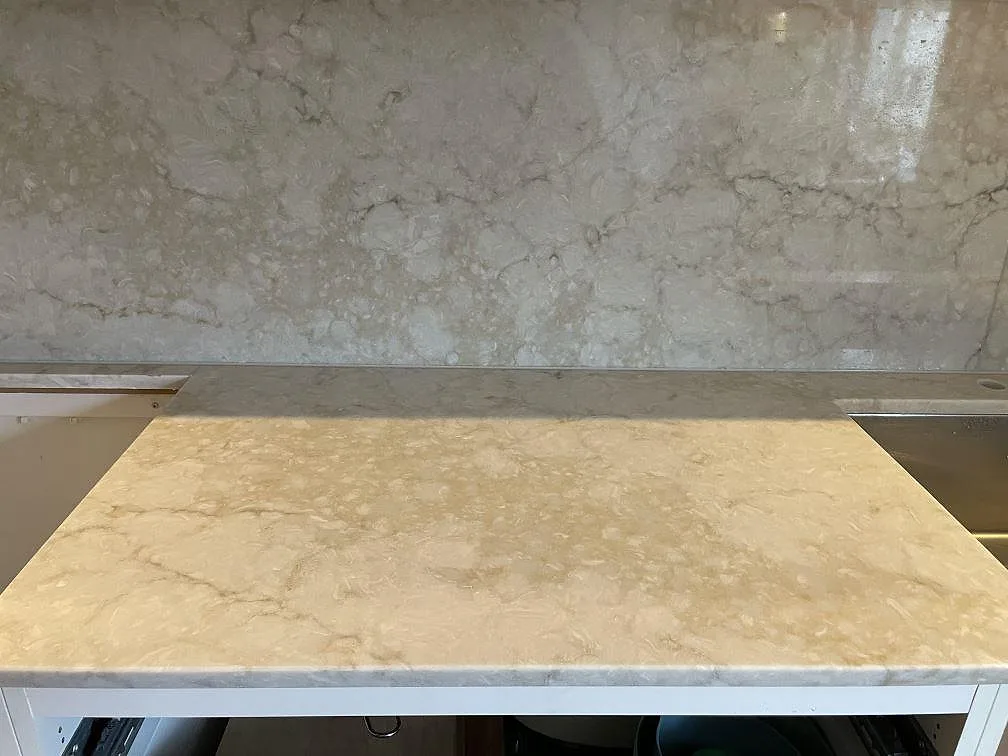Polerad köksbänkskiva i Royal Beige med varm beige yta och en heltäckande grå stänkvägg bakom, i ett kök i Uppsala fotograferat under montering.