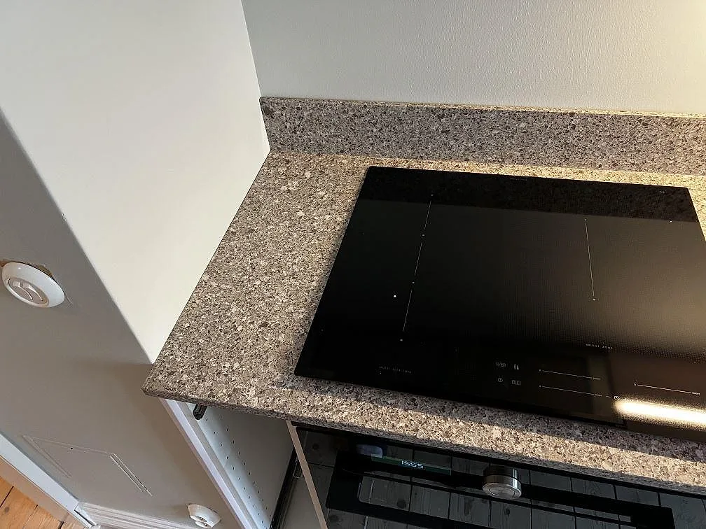 Sned vy över induktionshäll och uppvikt stänkkant i köksbänkskiva av polerad Silestone Alpina White i Göteborg.