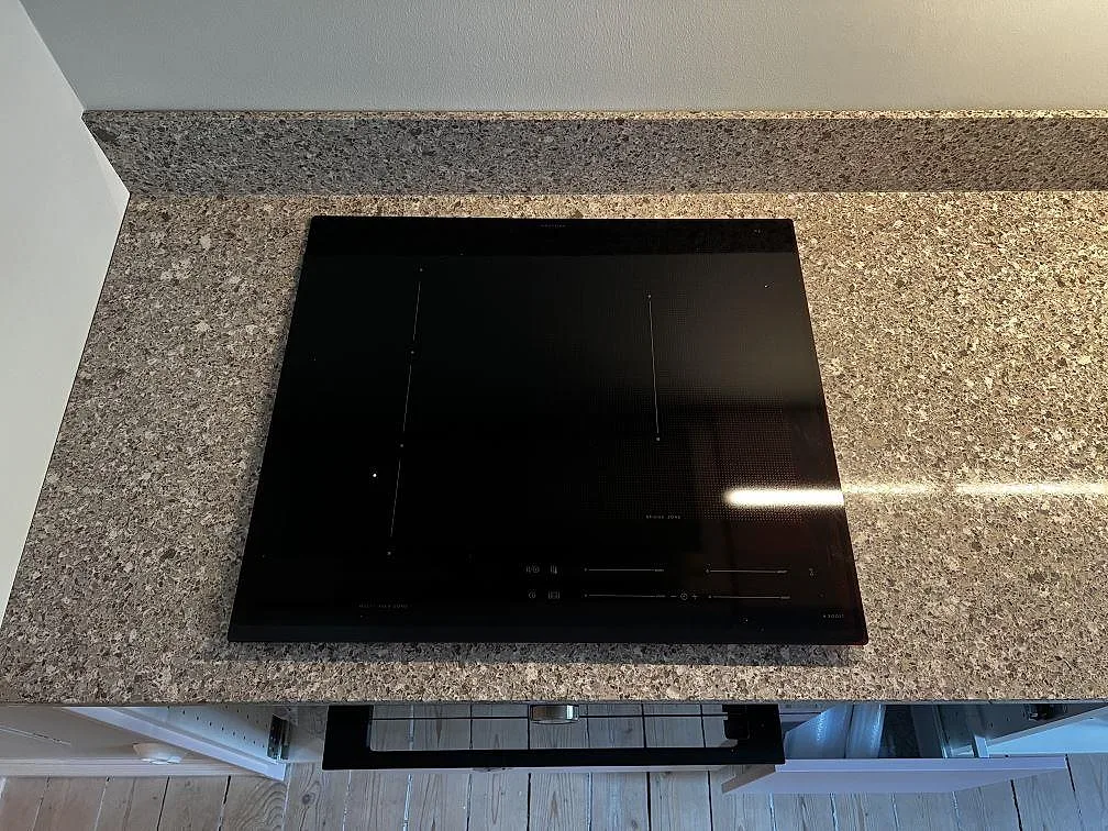 Närbild av svart induktionshäll i polerad Silestone Alpina White, med ljus reflektion i kompositytan i Göteborg.