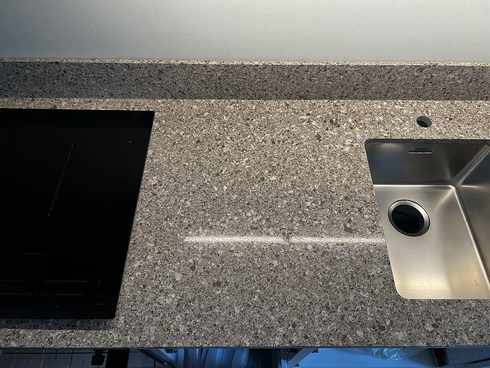 Detalj av polerad Silestone Alpina White med svart induktionshäll, underlimmad rostfri diskho och uppvikt stänkkant i Göteborg.