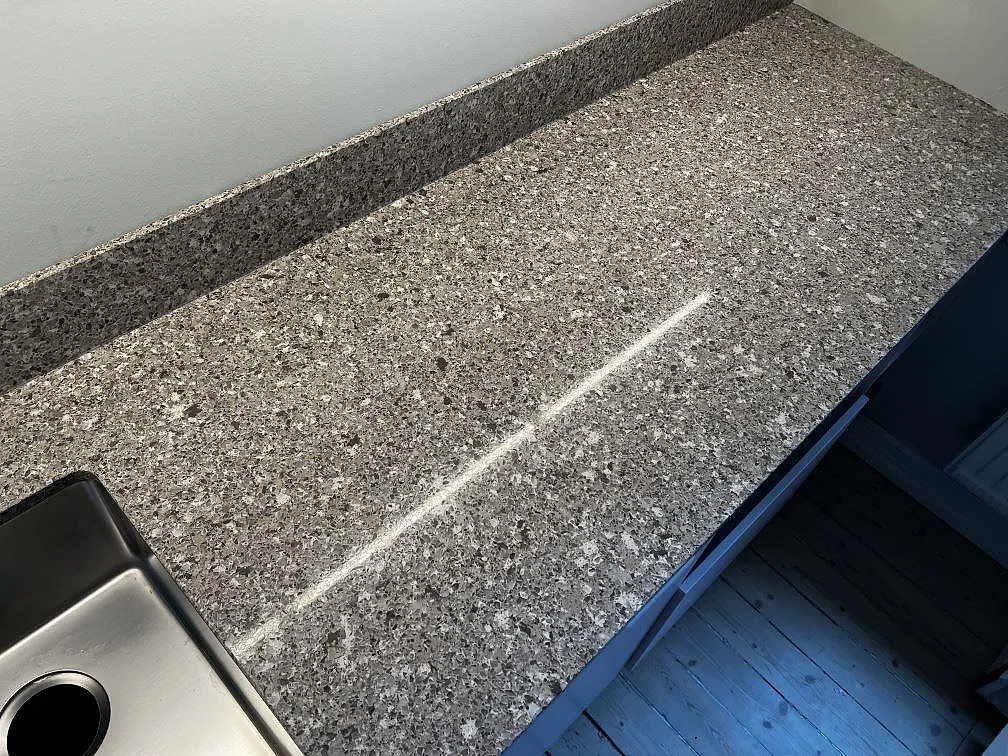 Lång arbetsyta i polerad Silestone Alpina White med grå terrazzo-liknande kompositstruktur och stänkkant i Göteborg.