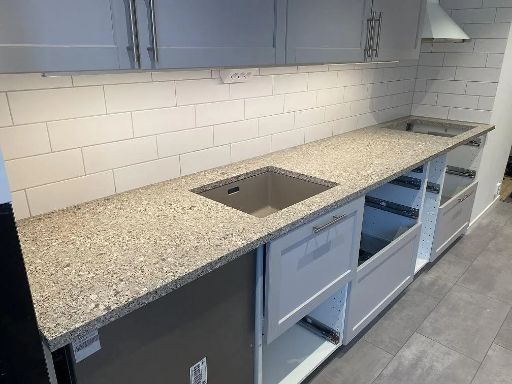 Lång köksbänk i polerad Silestone Alpina White med diskho och hällöppning i ett Malmö-kök under montering.